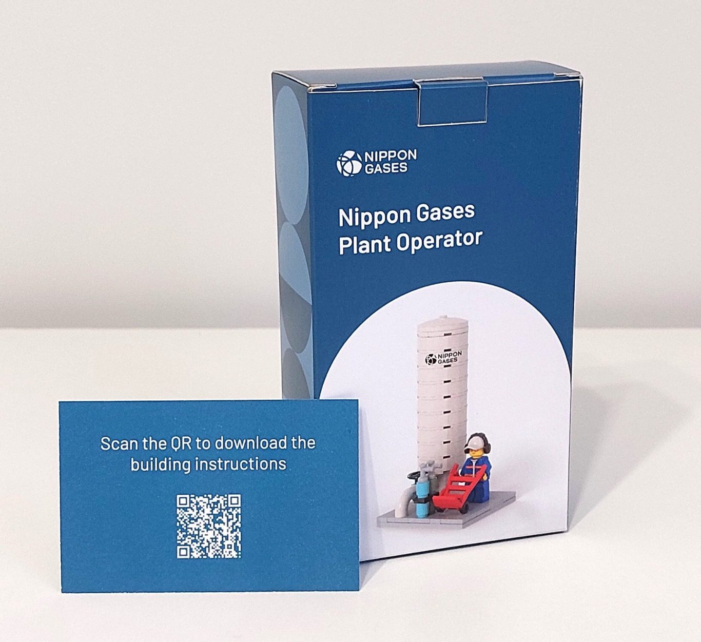 Regalos de empresa Lego Caja de juego "Nippon Gases" con una torre y figuras de operarios, junto a una tarjeta QR.